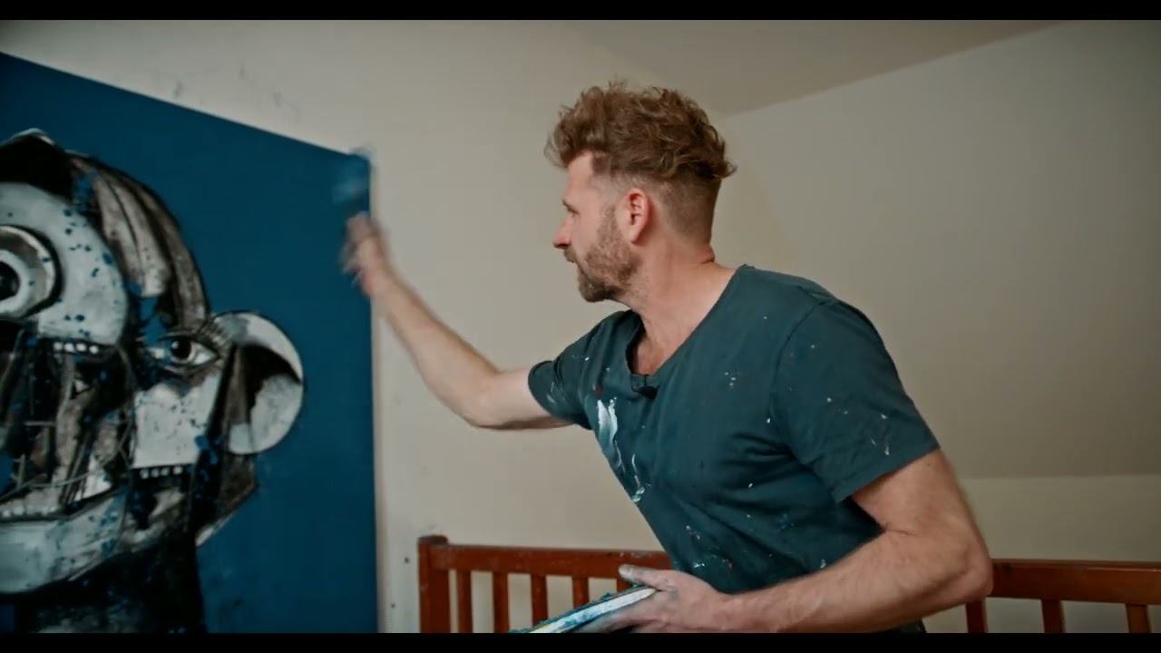 John Wren at work on a large blue canvas in his studio, in a paint-marked t-shirt.
